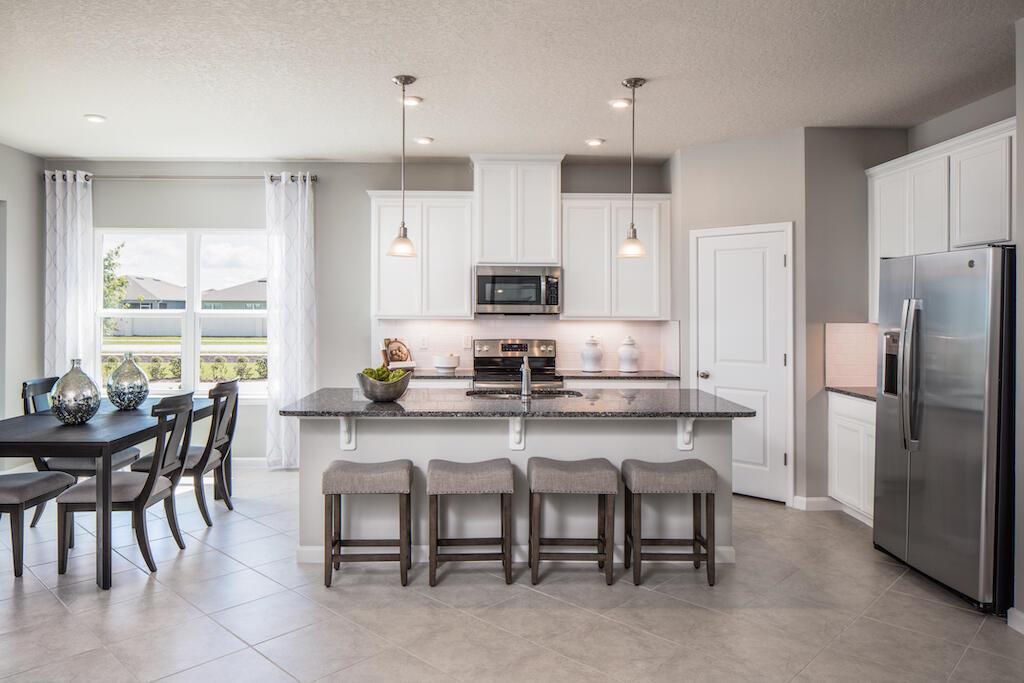 A kitchen features white cabinets, a granite-topped island with four stools, and stainless steel appliances — SEBASTIAN, FL