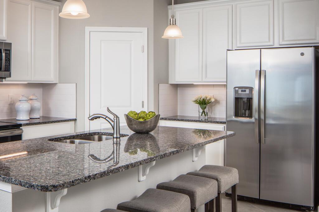 A kitchen features white cabinets, granite countertops, a center island with seating, and stainless appliances — SEBASTIAN, FL