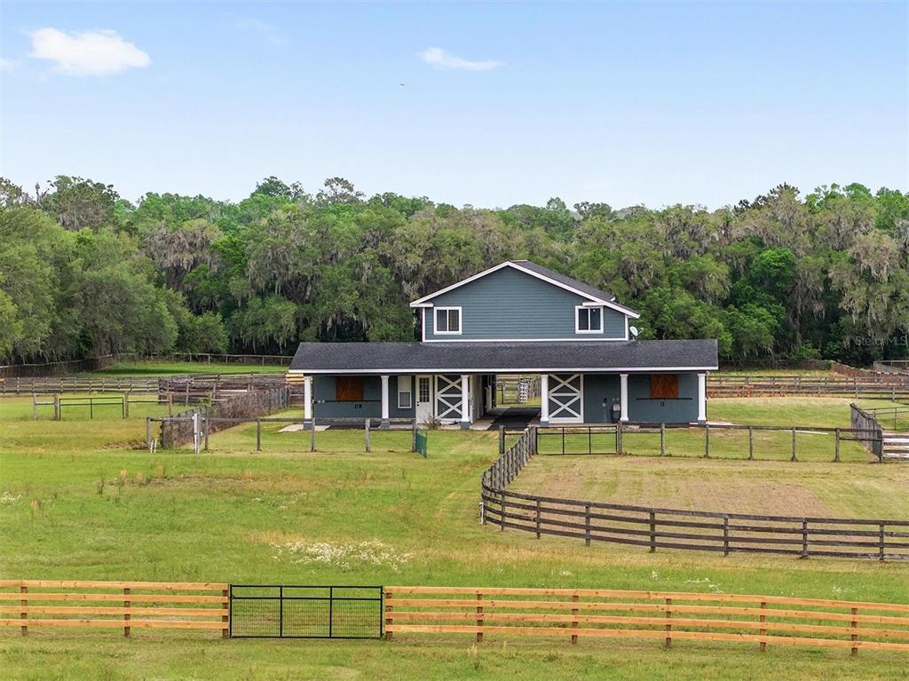 A blue two-story barn with horse stalls sits in a fenced pasture near a forest — 16201 NW 162ND TERRACE, WILLISTON, FL