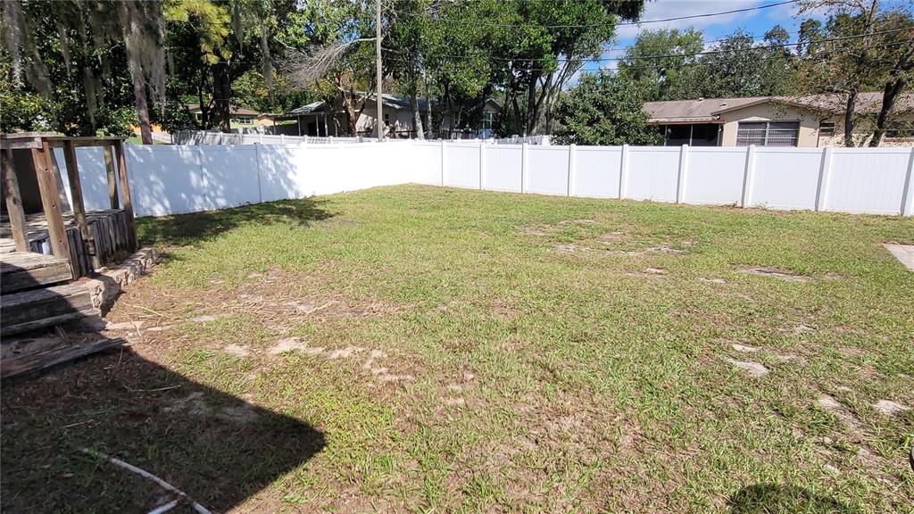 A fenced backyard features a grassy lawn and a wooden deck on the left side — 9 NEW YORK BOULEVARD, BEVERLY HILLS, FL