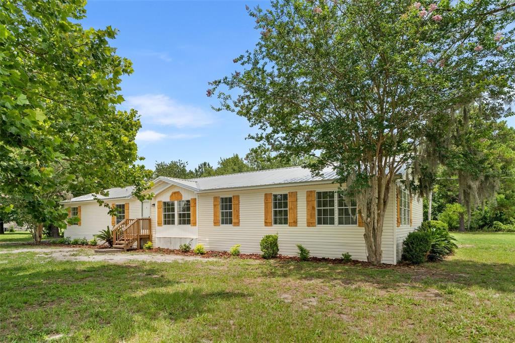 A single-story manufactured home with light siding, a metal roof, and wooden window shutters — 15591 NE 46TH STREET, WILLISTON, FL