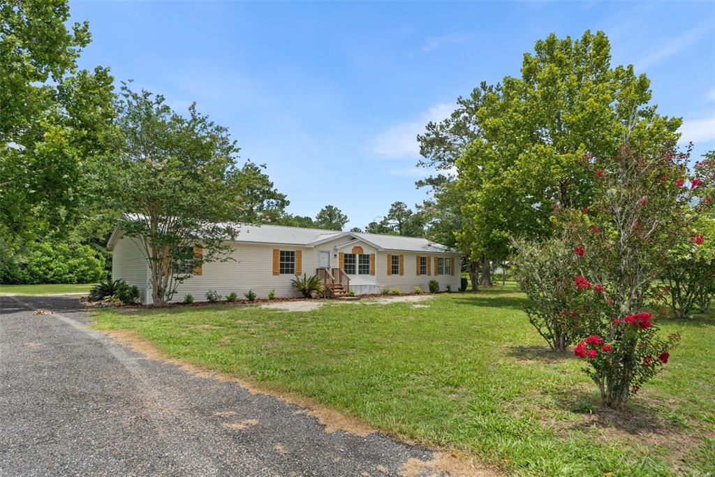 A single-story manufactured home with light siding and wooden shutters sits on a grassy lot — 15591 NE 46TH STREET, WILLISTON, FL