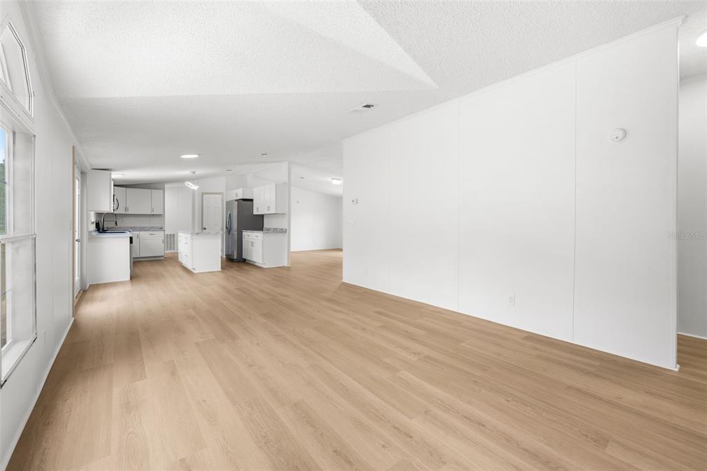 A bright, open-concept living area features light wood-look flooring and a white kitchen beyond — 15591 NE 46TH STREET, WILLISTON, FL