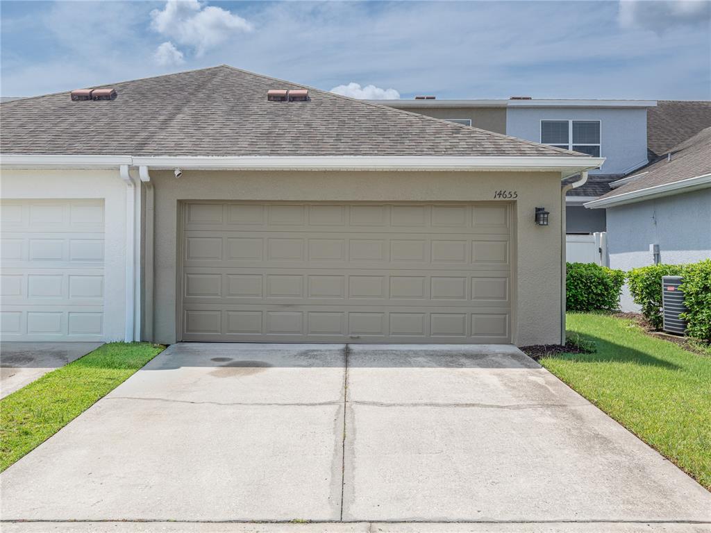 A tan garage with a concrete driveway and a white garage door to the left — 14655 WATER LOCUST DRIVE, ORLANDO, FL