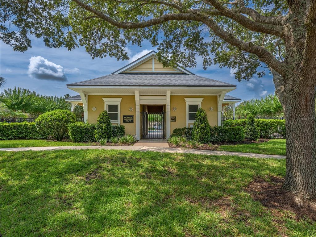A yellow community building with a gated entrance stands behind a lawn and large tree — 14655 WATER LOCUST DRIVE, ORLANDO, FL
