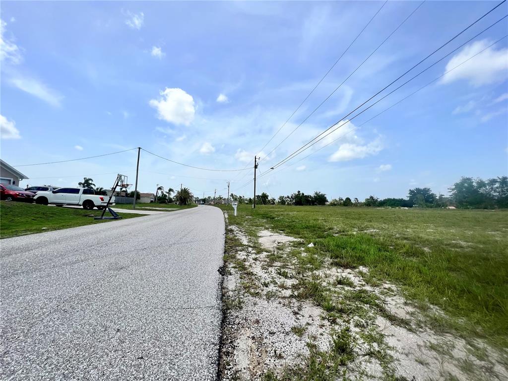 A paved road runs alongside a vacant grassy lot under a bright, partly cloudy sky — 3061 NW 5TH AVENUE, CAPE CORAL, FL