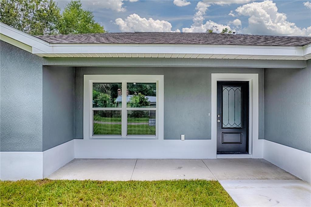 A gray house exterior features a covered porch, a black front door, and a window — 557 COUNTY ROAD 487, LAKE PANASOFFKEE, FL