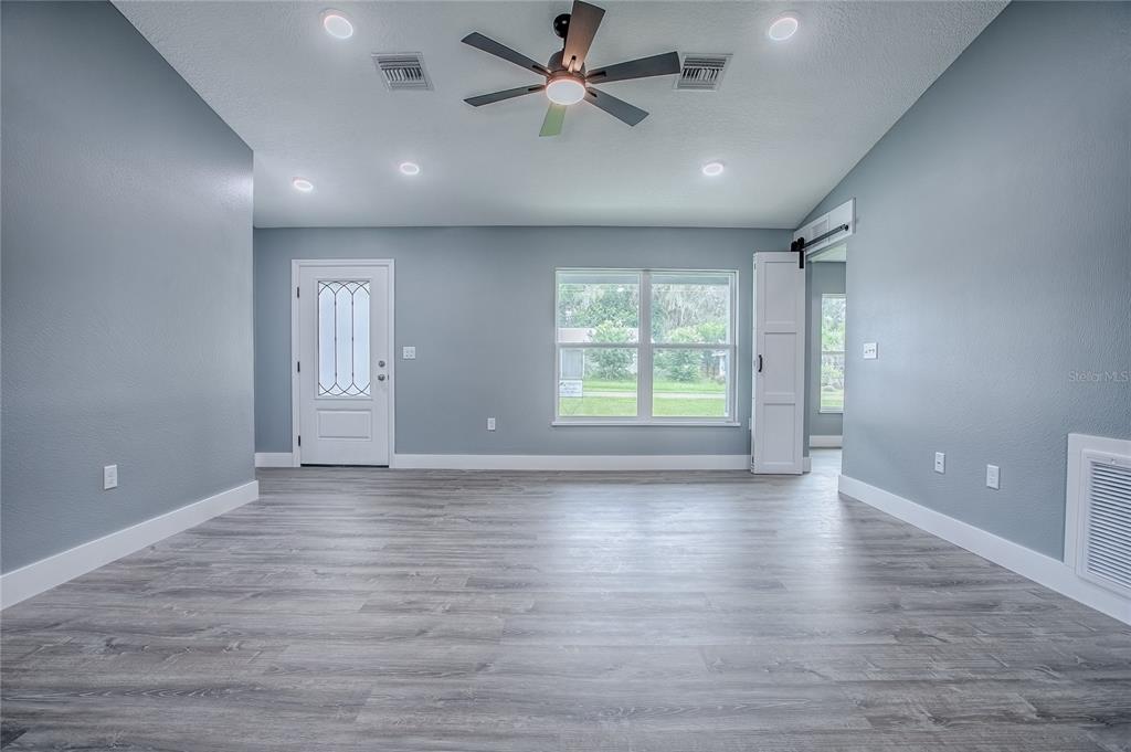 A living room features gray walls, wood-look flooring, a ceiling fan, and a white door — 557 COUNTY ROAD 487, LAKE PANASOFFKEE, FL