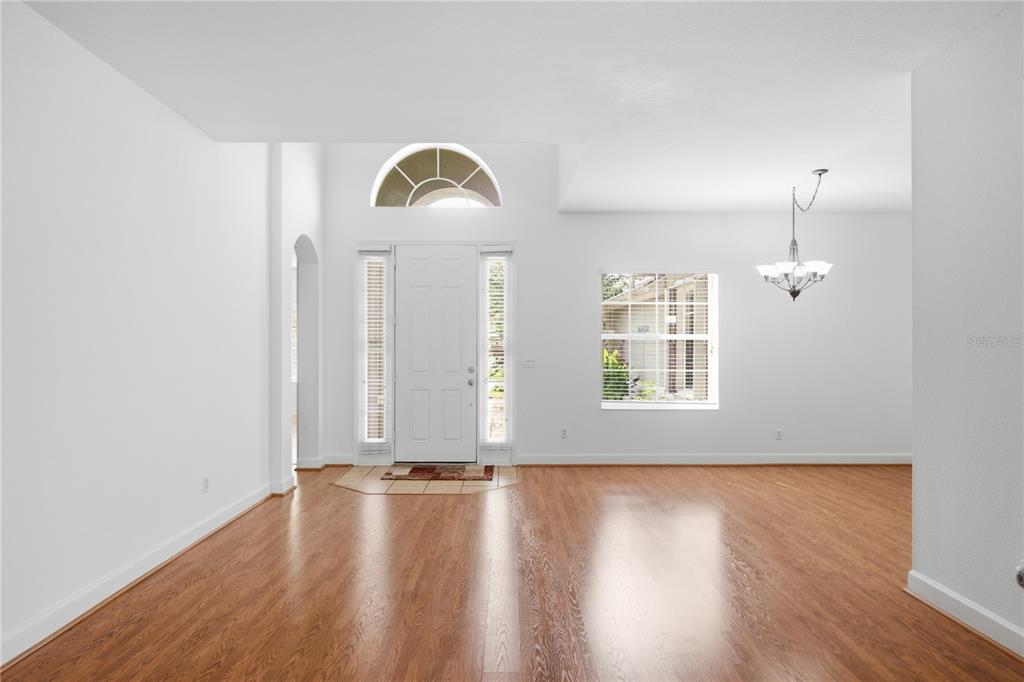 A bright, empty foyer features hardwood floors, a high ceiling, and a white front door — 3476 FOREST RIDGE LANE, KISSIMMEE, FL