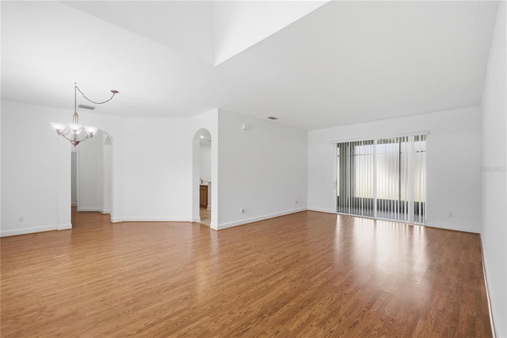 A spacious, empty living room with light wood flooring, white walls, and a sliding glass door — 3476 FOREST RIDGE LANE, KISSIMMEE, FL
