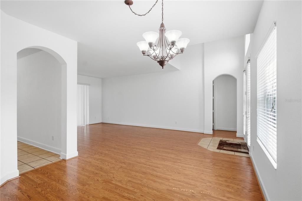 A bright, empty dining room features wood-look flooring, a chandelier, and arched doorways — 3476 FOREST RIDGE LANE, KISSIMMEE, FL