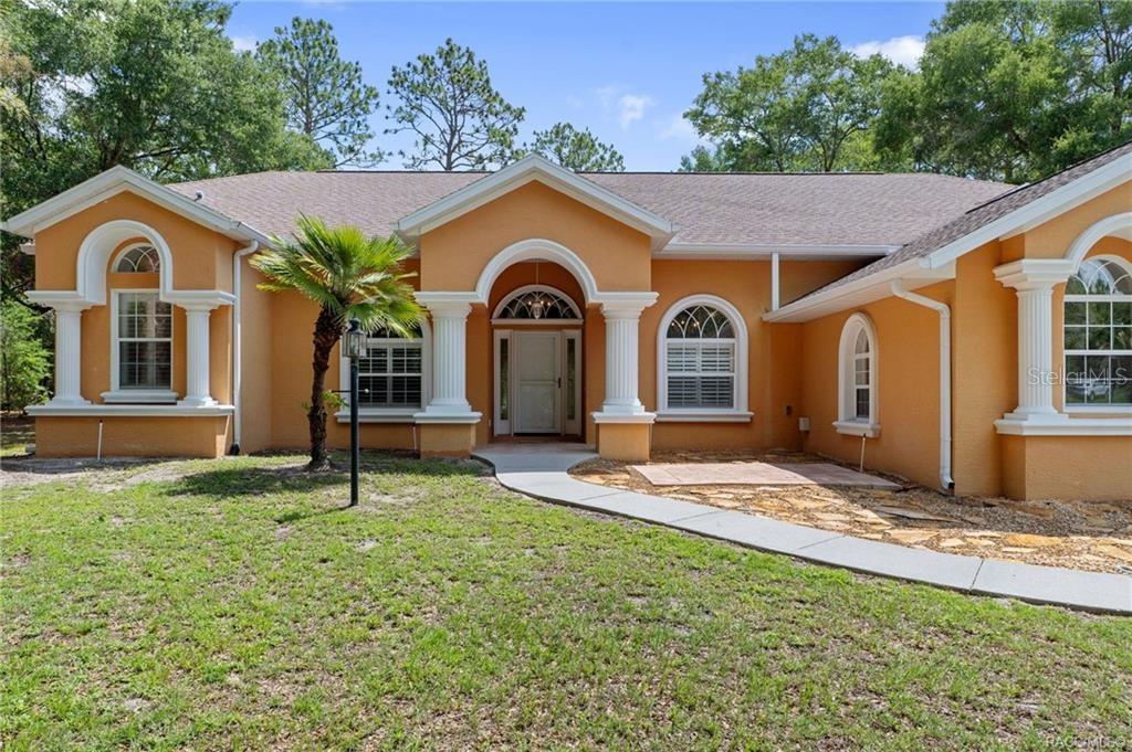 A single-story orange stucco house features white columns, arched windows, and a concrete walkway — 7145 SW 181ST AVENUE, DUNNELLON, FL
