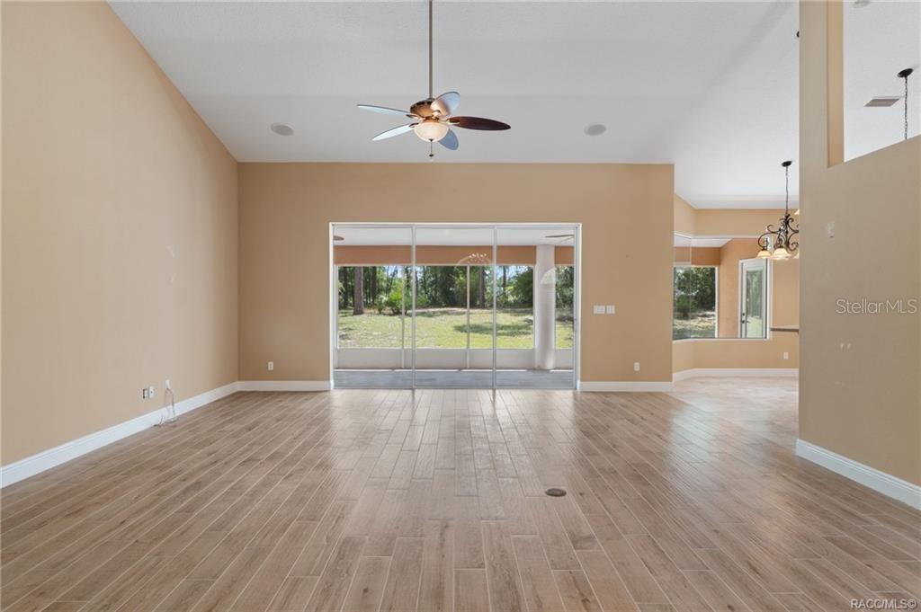 A spacious living room features light wood-look tile flooring, tan walls, and sliding glass doors — 7145 SW 181ST AVENUE, DUNNELLON, FL