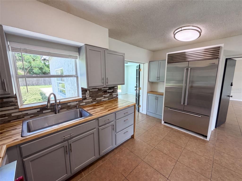 A kitchen features gray cabinets, butcher block countertops, a stainless steel refrigerator, and tile flooring — 1907 SUE ANN STREET, ORLANDO, FL