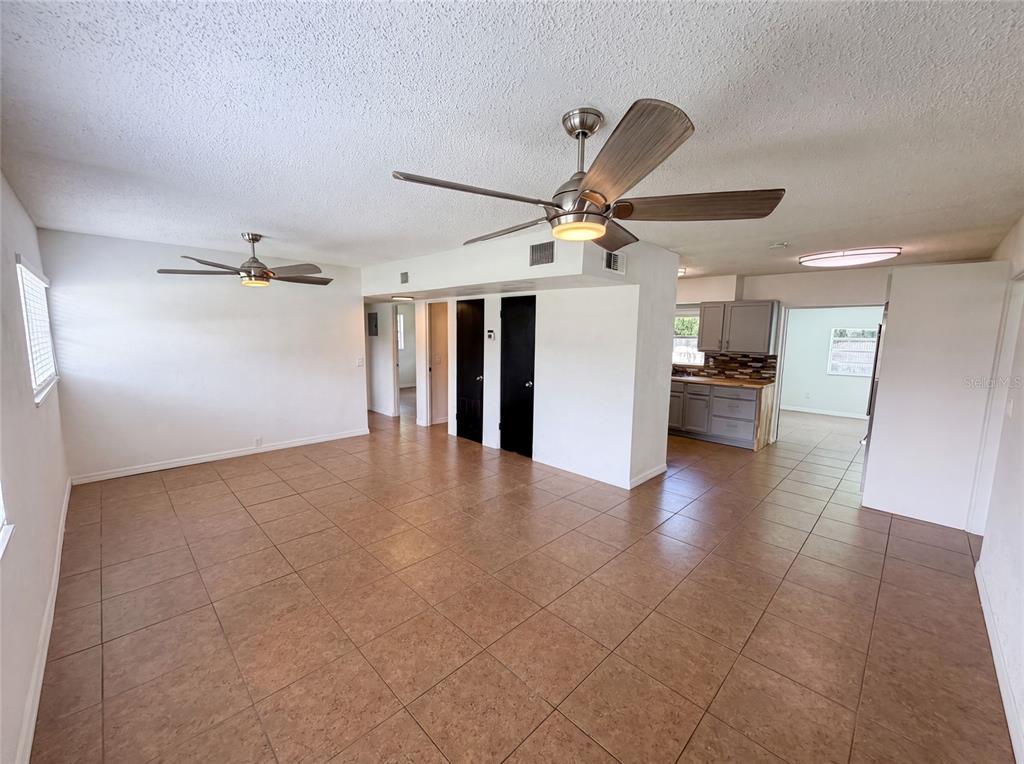 A spacious room with tile flooring, two ceiling fans, and a view of the kitchen — 1907 SUE ANN STREET, ORLANDO, FL