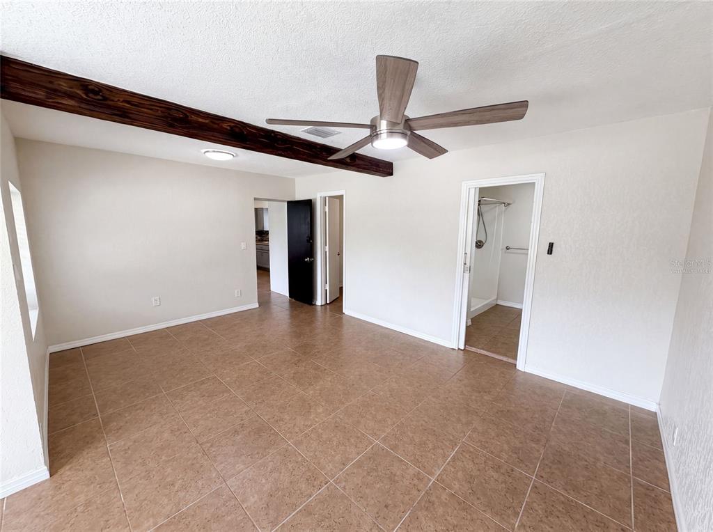 An empty room features tiled floors, a wooden ceiling beam, and a ceiling fan — 1907 SUE ANN STREET, ORLANDO, FL