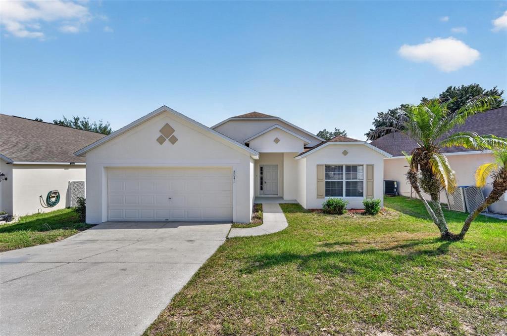 A single-story house with a white stucco exterior, a two-car garage, and a palm tree — 2041 NEWTOWN ROAD, GROVELAND, FL