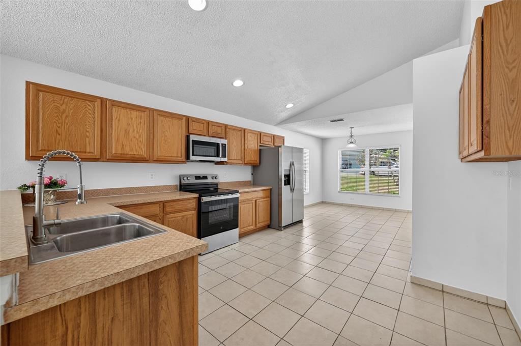 A kitchen with oak cabinets, stainless steel appliances, and tile flooring opens to a dining area — 2041 NEWTOWN ROAD, GROVELAND, FL