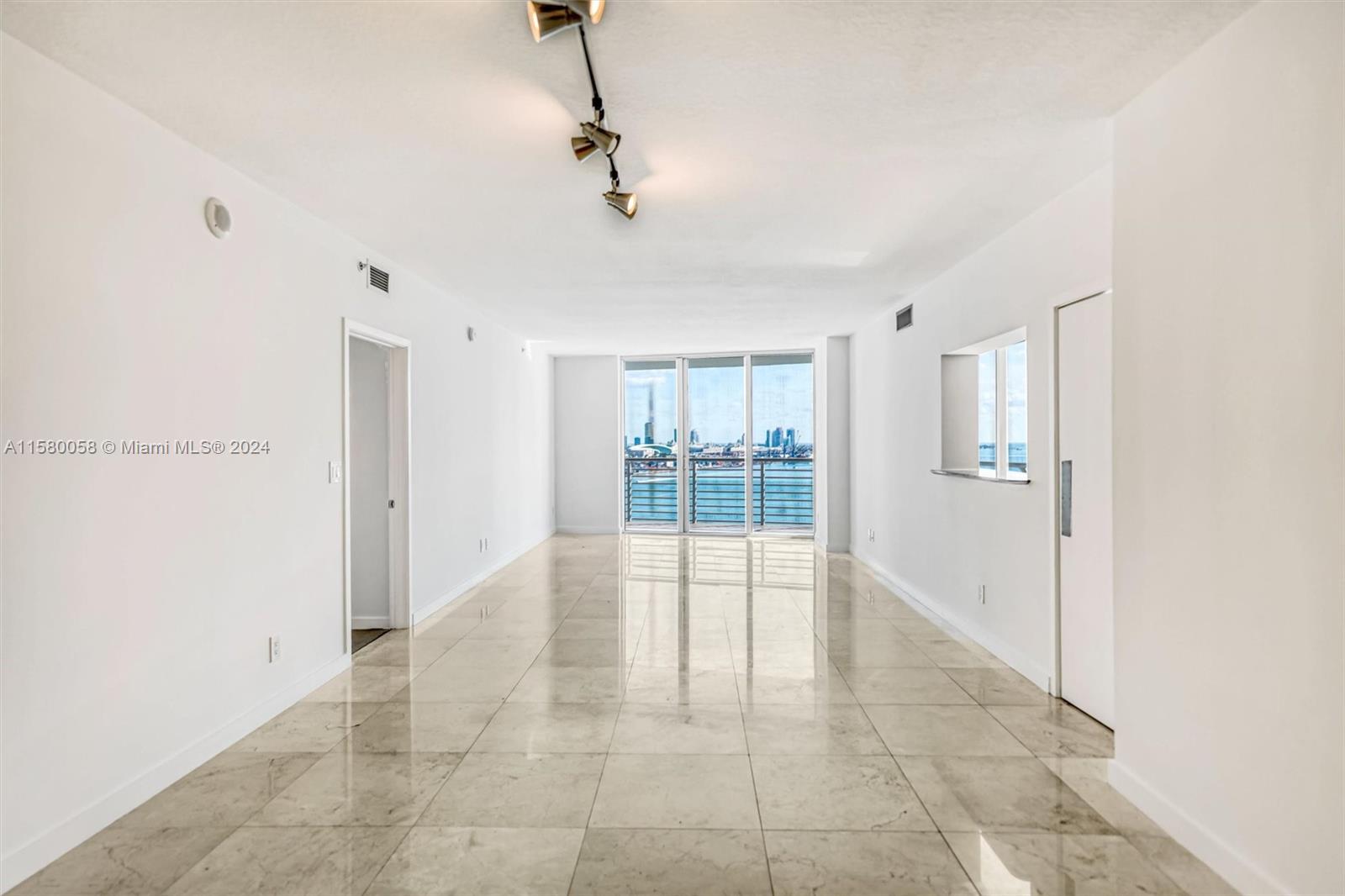 An empty room with light-colored tile flooring features a track light and a balcony view — 325 NE Biscayne Blvd # 1923, Miami FL 33131, MIAMI, FL