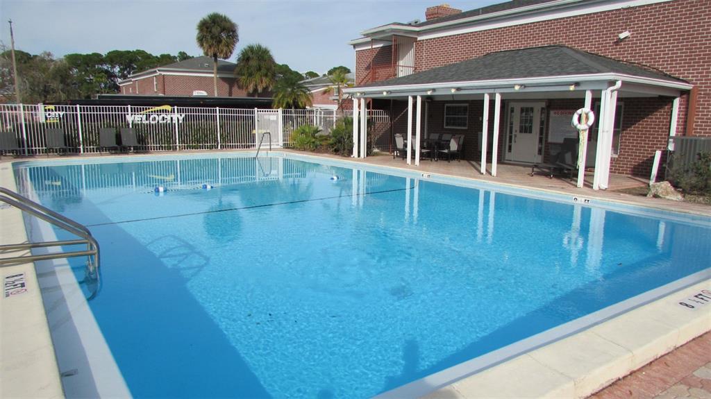 A rectangular swimming pool sits in front of a brick building with a covered patio — 8500 13TH STREET N UNIT A, ST PETERSBURG, FL