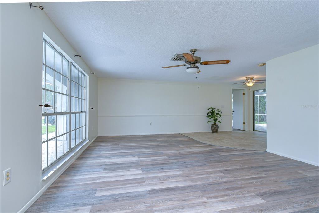 A living room with wood-look flooring, a ceiling fan, and a large window — 8804 VILLAGE MILL ROW, HUDSON, FL