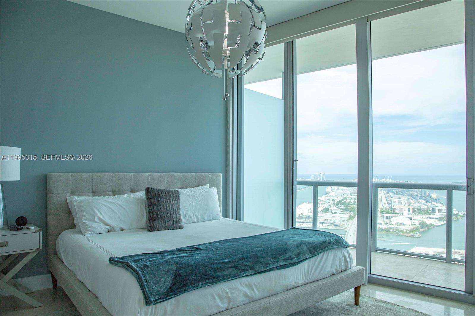 A bedroom features a bed with a blue throw, a modern chandelier, and floor-to-ceiling windows — 888 Biscayne Blvd # 5207, Miami FL 33132, MIAMI, FL