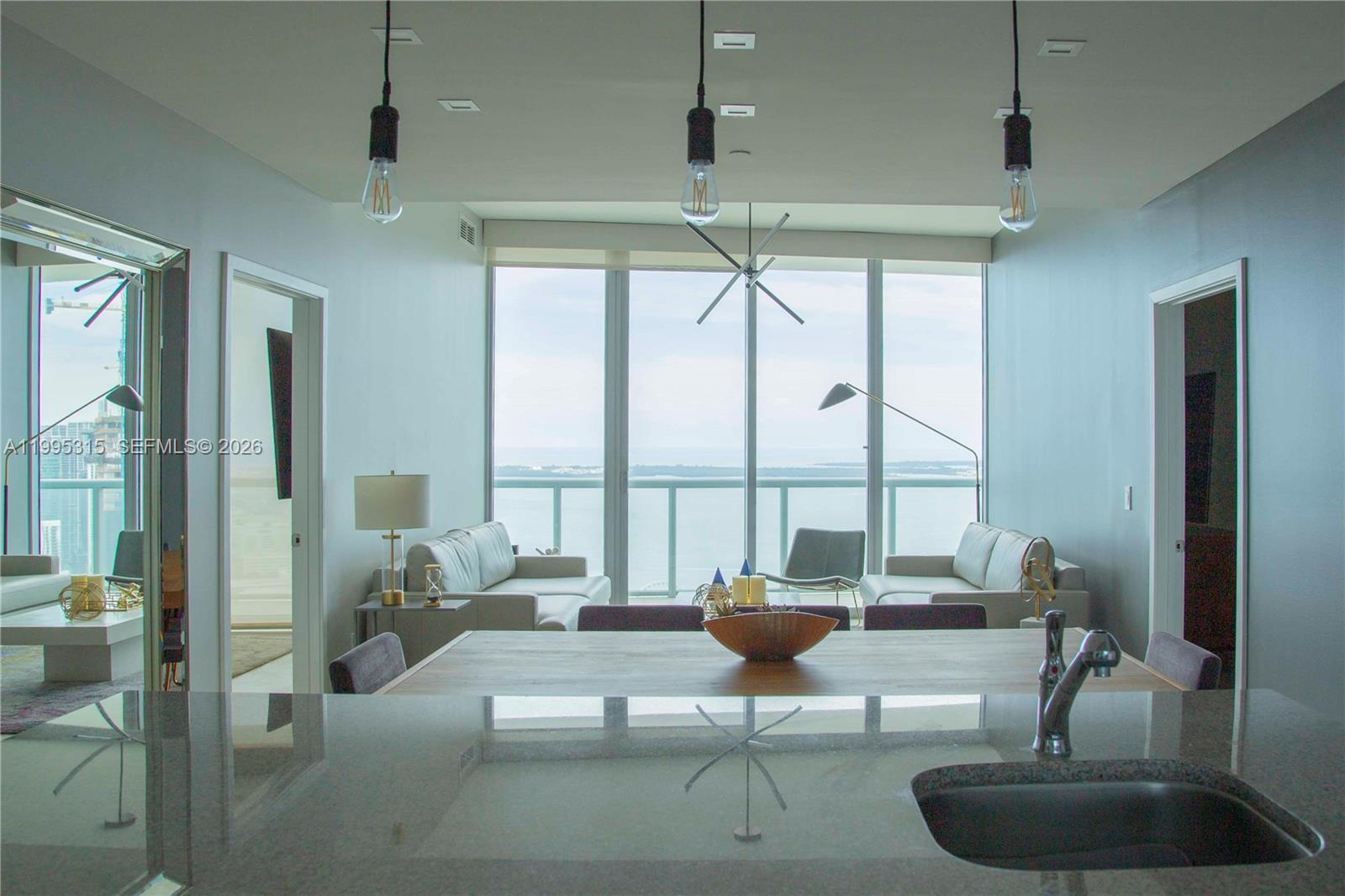 A kitchen island overlooks a living area with floor-to-ceiling windows and a water view — 888 Biscayne Blvd # 5207, Miami FL 33132, MIAMI, FL