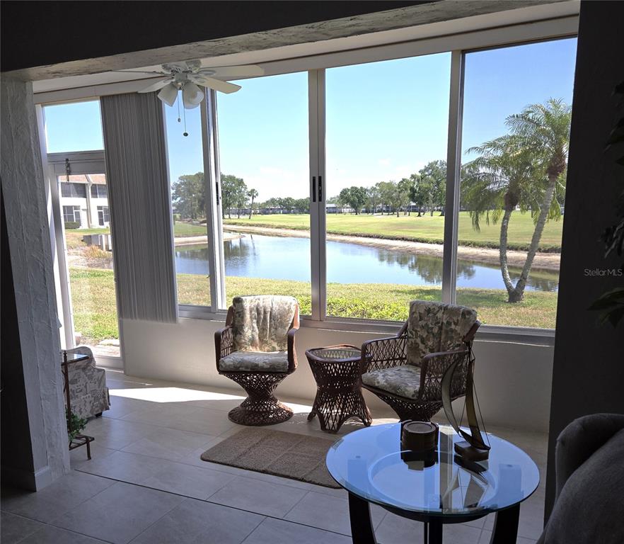 A sunroom features tile flooring, wicker furniture, and large windows overlooking a pond and golf course — 7193 W COUNTRY CLUB DRIVE N UNIT 138, SARASOTA, FL