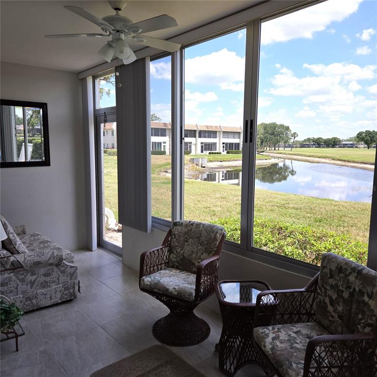 A sunroom with tile floors, wicker chairs, and large windows overlooking a pond and golf course — 7193 W COUNTRY CLUB DRIVE N UNIT 138, SARASOTA, FL