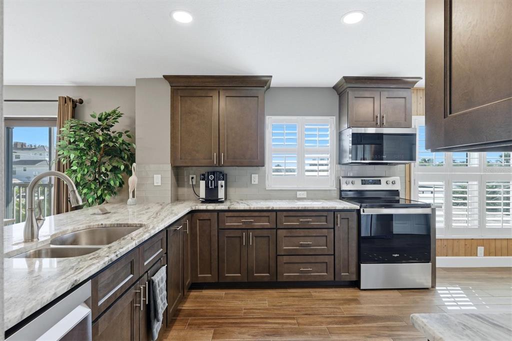 A kitchen features dark wood cabinets, granite countertops, stainless steel appliances, and wood-look flooring — 1001 BENJAMIN FRANKLIN DRIVE UNIT 206, SARASOTA, FL