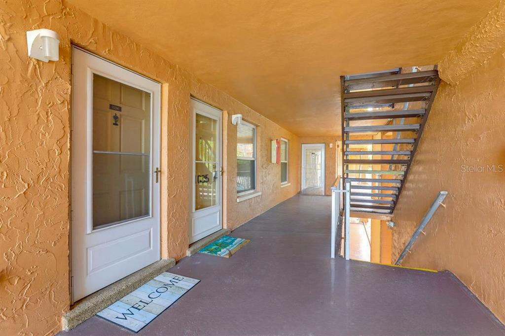 An outdoor apartment walkway features two white doors, a staircase, and orange stucco walls — 12760 INDIAN ROCKS ROAD UNIT 1034, LARGO, FL