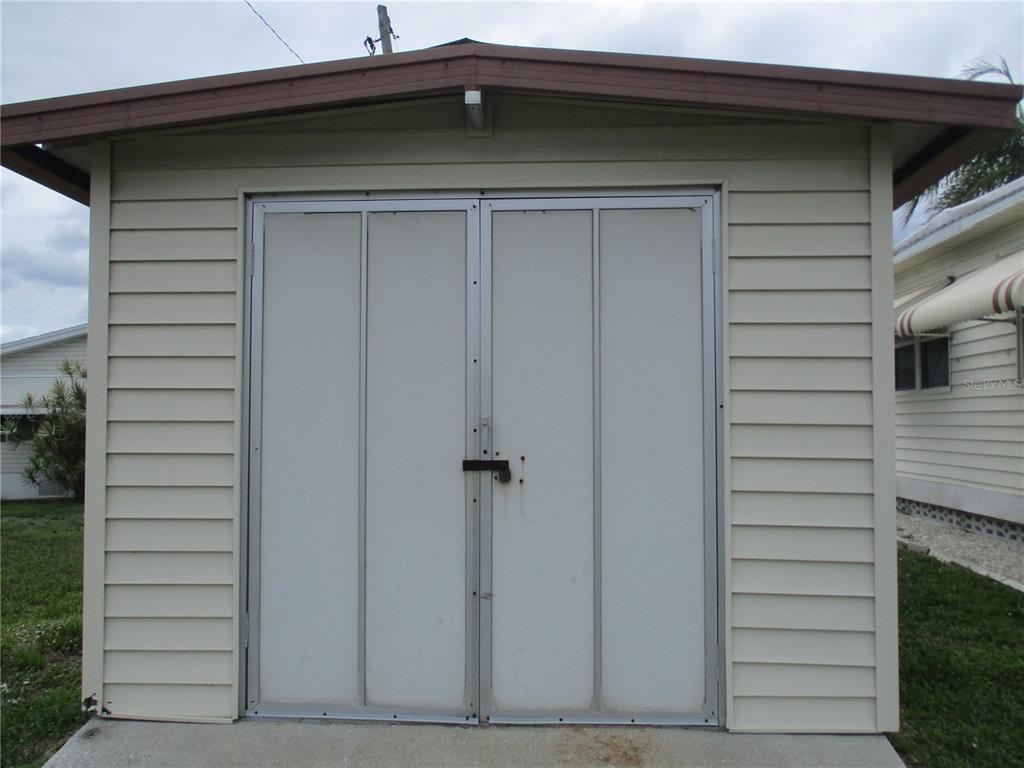 A beige storage shed with double doors and a brown roof stands on a concrete pad — 5009 8TH B STREET E, BRADENTON, FL