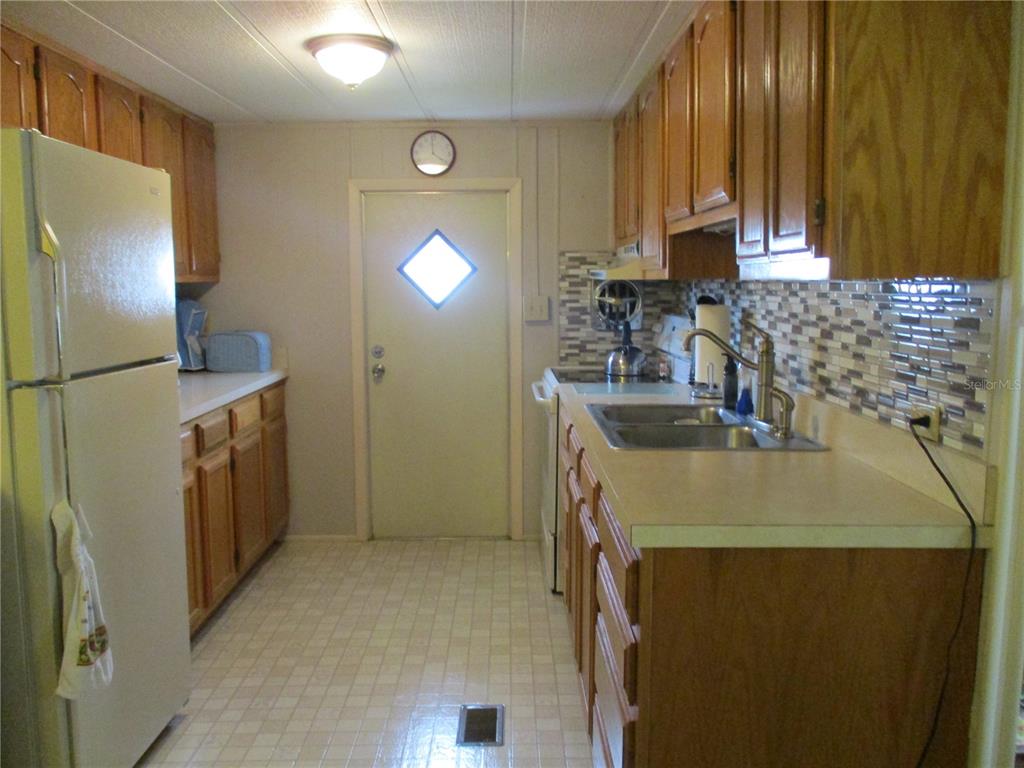 A galley kitchen features wood cabinets, laminate countertops, a tiled backsplash, and a white refrigerator — 5009 8TH B STREET E, BRADENTON, FL