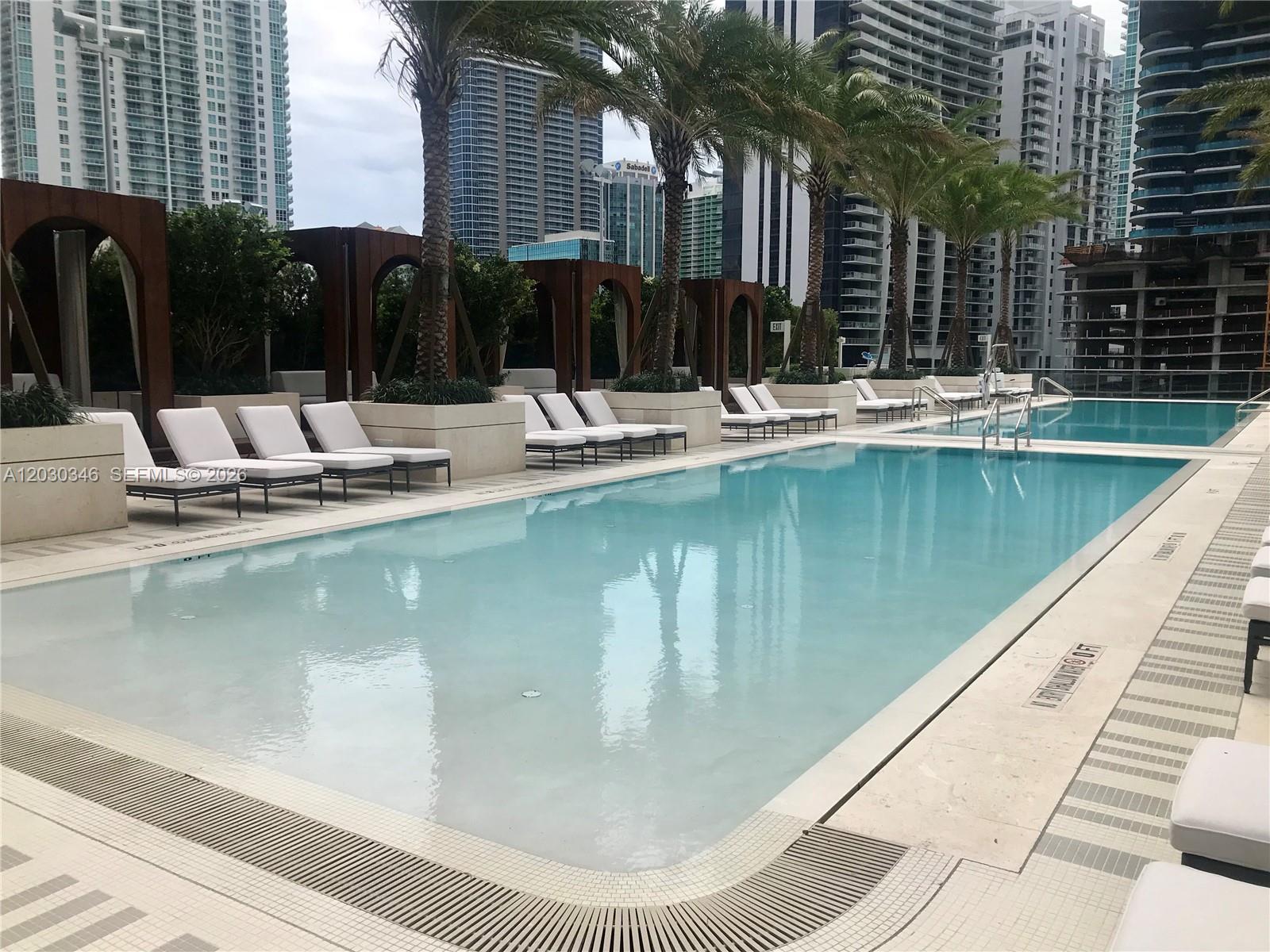 An outdoor swimming pool surrounded by lounge chairs, palm trees, and modern high-rise buildings — 801 S Miami Ave # 1502, Miami FL 33130, MIAMI, FL