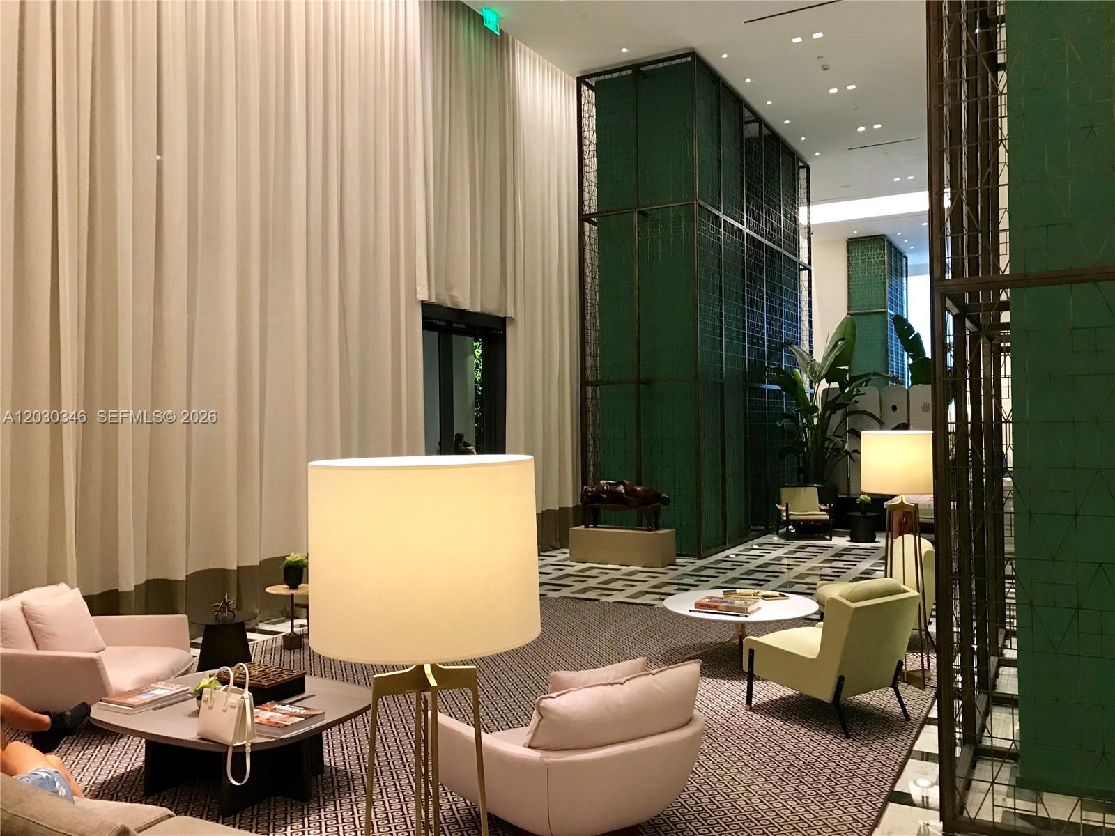 A modern lobby features tall white curtains, green metal partitions, and contemporary lounge furniture — 801 S Miami Ave # 1502, Miami FL 33130, MIAMI, FL