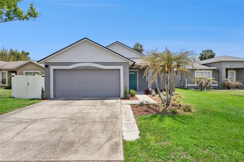 A single-story house with a gray garage, a teal front door, and a palm tree — 1189 AMANDA KAY CIRCLE, SANFORD, FL