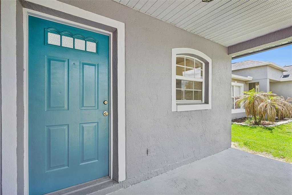 A teal front door with a window sits next to a window on a porch — 1189 AMANDA KAY CIRCLE, SANFORD, FL