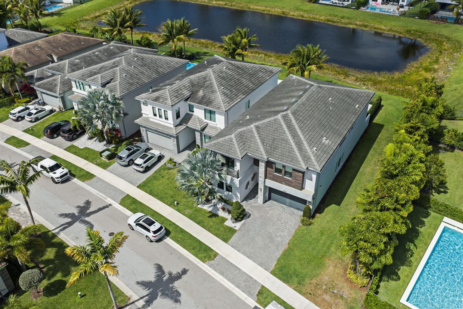 An aerial view shows several suburban houses with tiled roofs, driveways, and a nearby pond — 8599 Tower Bridge Court, Boca Raton FL 33496, BOCA RATON, FL