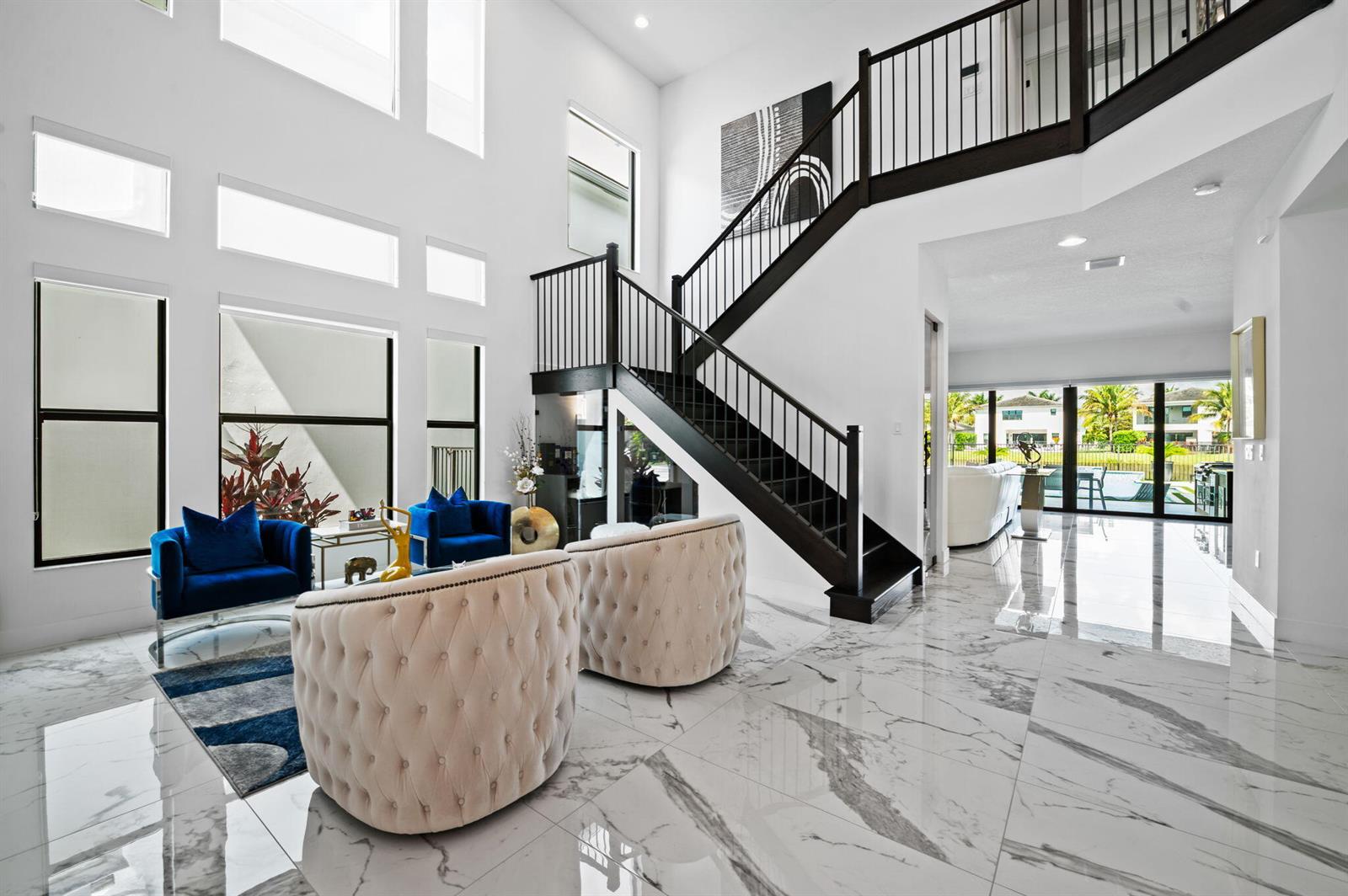 A bright, two-story foyer features marble floors, a dark wood staircase, and modern seating areas — 8599 Tower Bridge Court, Boca Raton FL 33496, BOCA RATON, FL