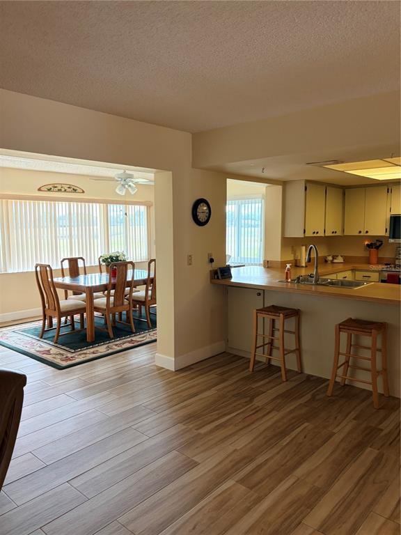 An open-concept kitchen with a breakfast bar overlooks a dining area with wood-look tile flooring — 2117 HARLESTON UNIT 2117, SUN CITY CENTER, FL