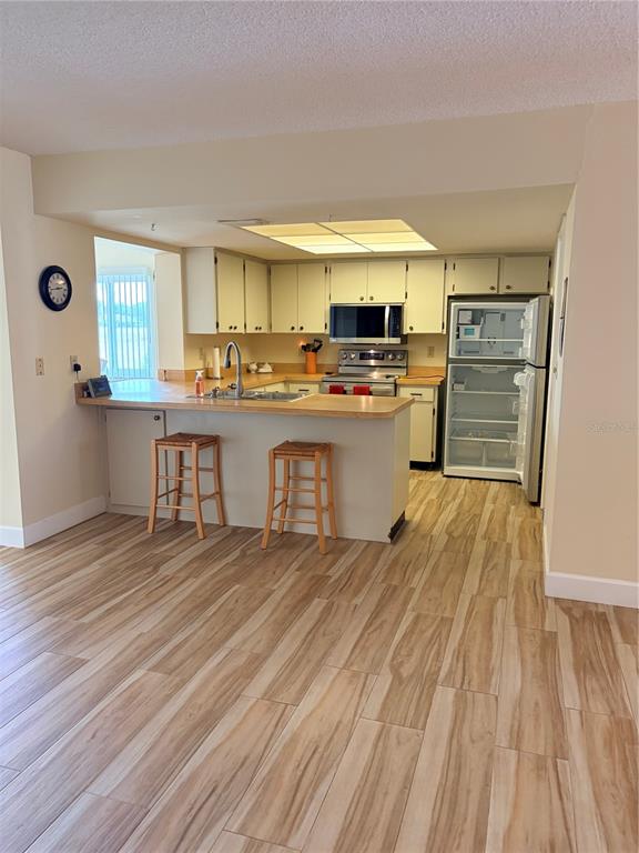 A kitchen features light-colored cabinets, a breakfast bar with two stools, and wood-look tile flooring — 2117 HARLESTON UNIT 2117, SUN CITY CENTER, FL
