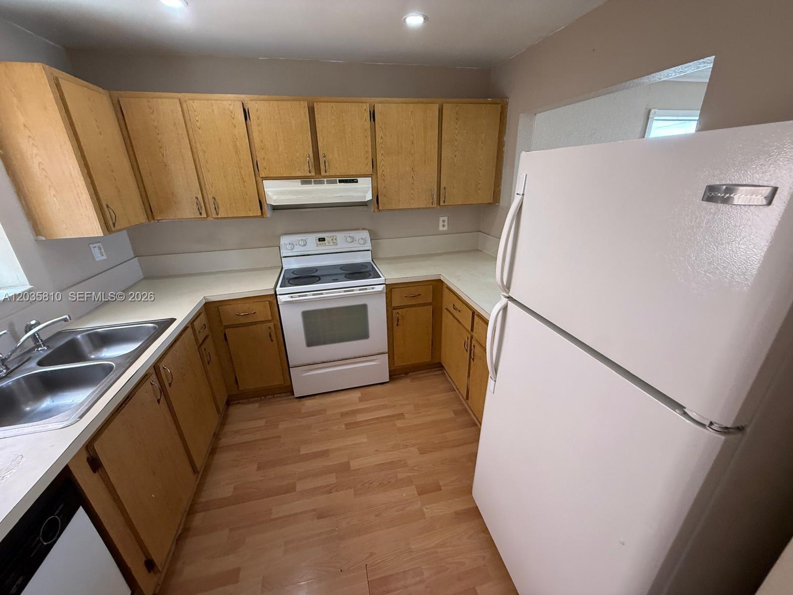 A kitchen features light wood cabinets, white appliances, laminate countertops, and wood-look flooring — 6175 W 20th Ave # 210, Hialeah FL 33012, HIALEAH, FL