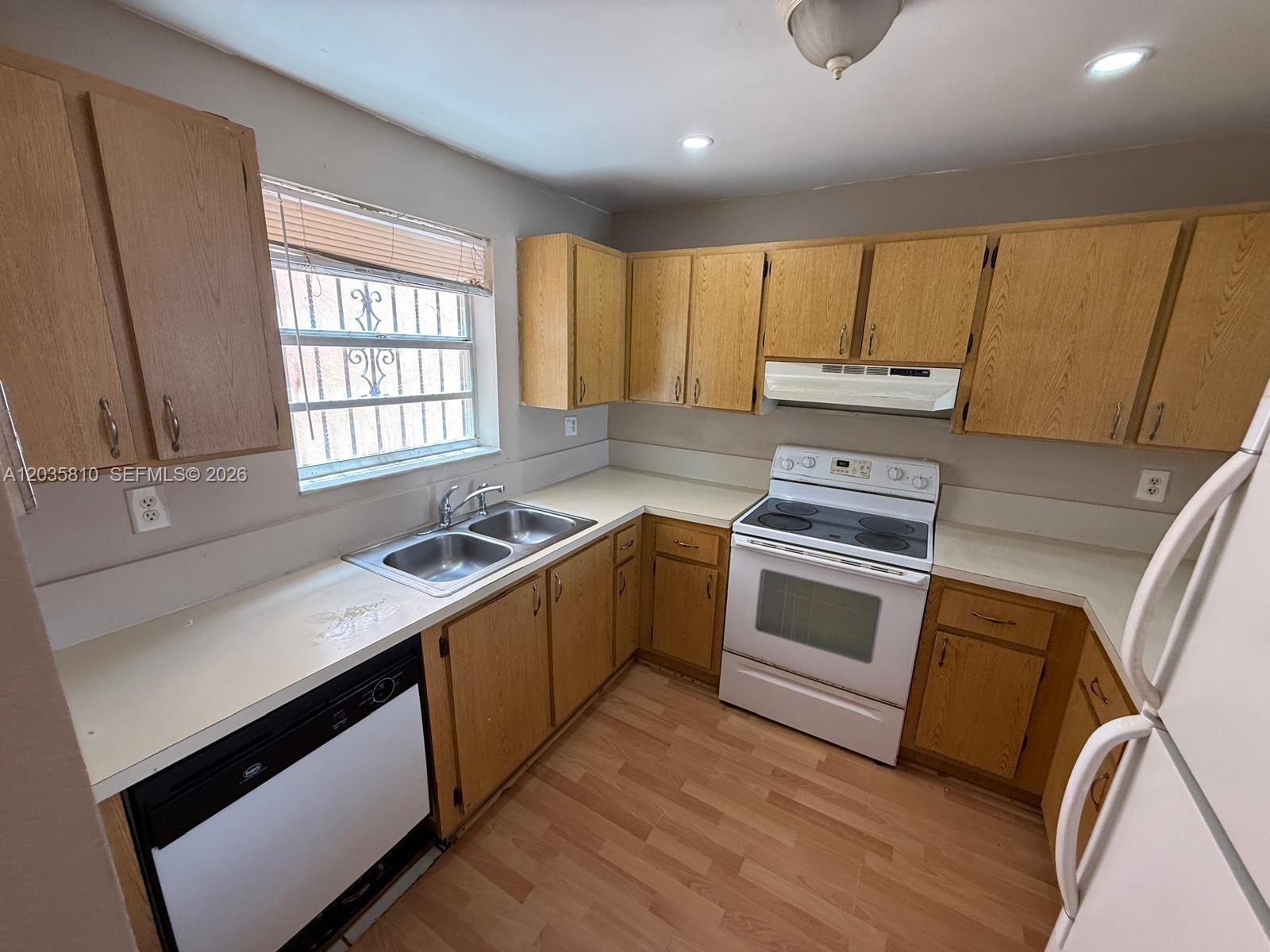 A kitchen features oak cabinets, white appliances, a double sink, and light wood-look flooring — 6175 W 20th Ave # 210, Hialeah FL 33012, HIALEAH, FL