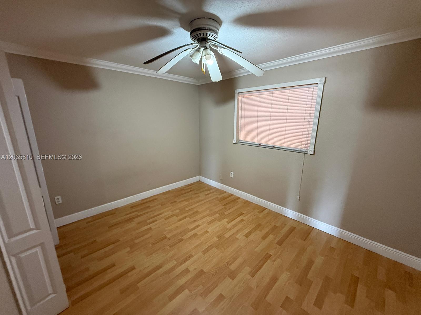 An empty bedroom features light-colored wood flooring, beige walls, a ceiling fan, and a window — 6175 W 20th Ave # 210, Hialeah FL 33012, HIALEAH, FL