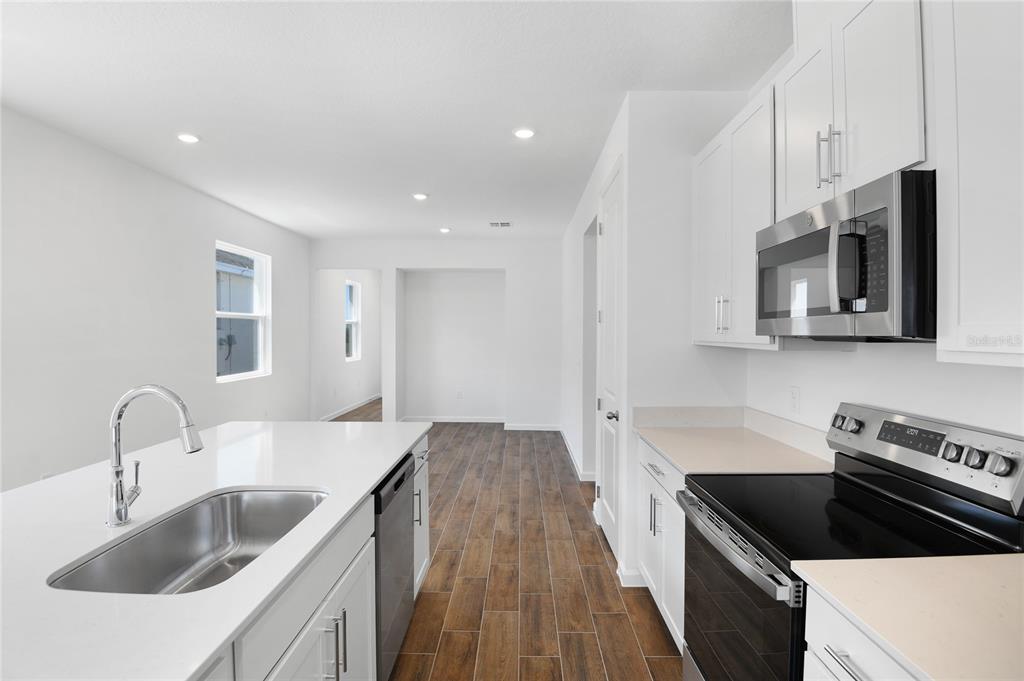 A modern kitchen features white cabinets, stainless steel appliances, a center island, and wood-look flooring — 6373 CLOVER STREET, LAKE HAMILTON, FL