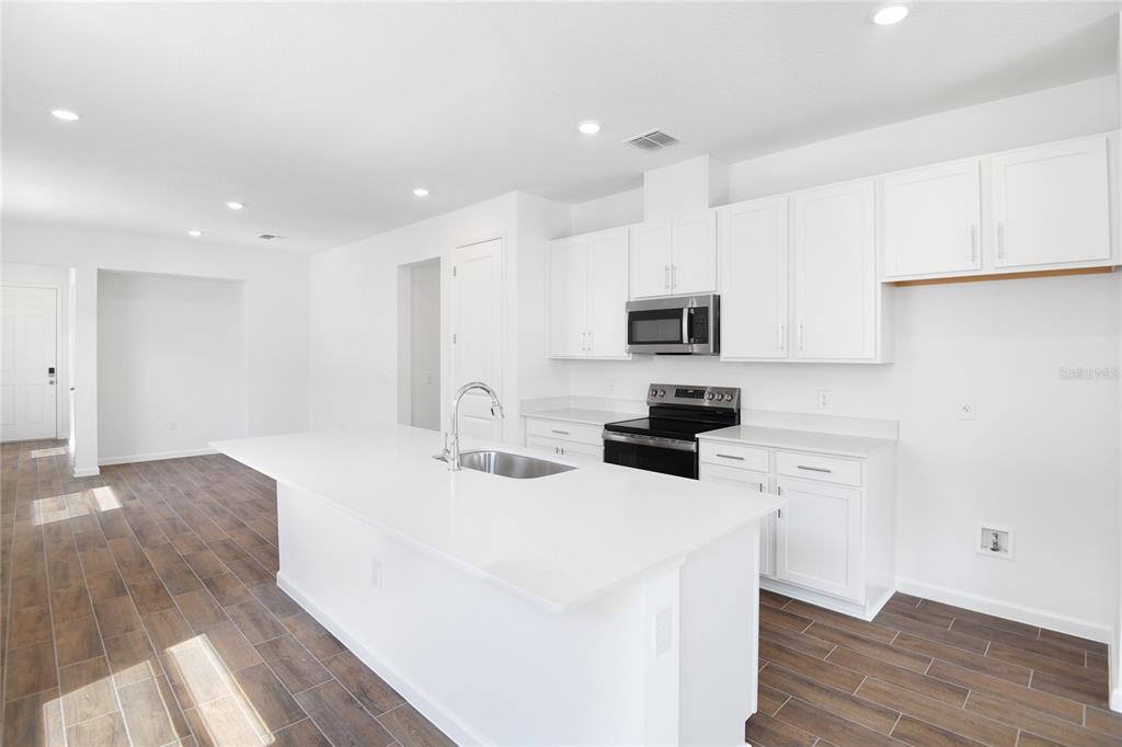 A modern kitchen features white cabinets, a large island with a sink, and wood-look flooring — 6373 CLOVER STREET, LAKE HAMILTON, FL