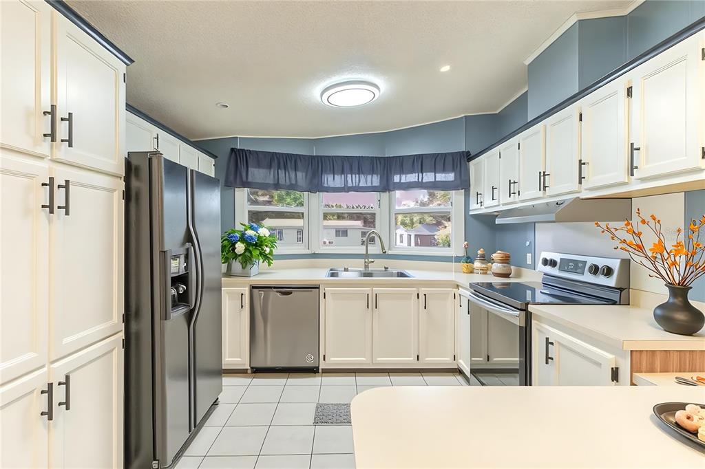 A kitchen features white cabinets, stainless steel appliances, a bay window, and light tile flooring — 2510 ISLAND OAKS E, LAKELAND, FL