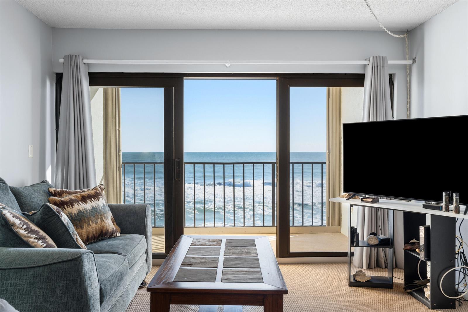 A living room features a sofa, coffee table, television, and sliding doors overlooking the ocean — 10310 S Ocean Drive # 609, Jensen Beach FL 34957, JENSEN BEACH, FL