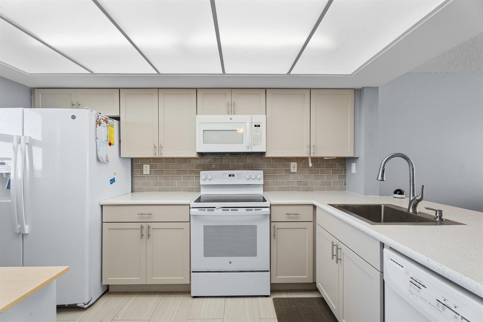 A kitchen features light-colored cabinets, white appliances, a tiled backsplash, and a drop-in sink — 10310 S Ocean Drive # 609, Jensen Beach FL 34957, JENSEN BEACH, FL