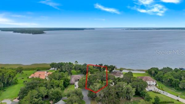 An aerial view shows a vacant, tree-covered lot outlined in red along a large lake — 716 NEWELL HILL RD, LEESBURG, FL